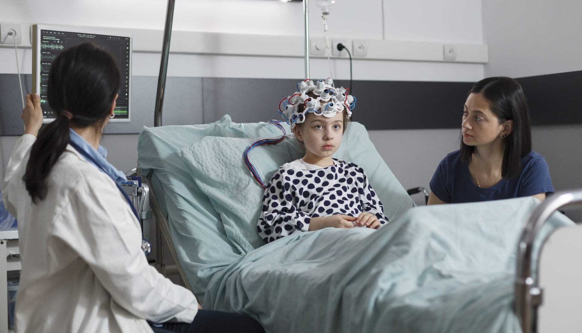 Expert pediatrician monitoring hospitalized girl brain condition using EEG headset. Neurology specialist measuring neurologic disease evolution of sick kid sitting in pediatric healthcare facility.